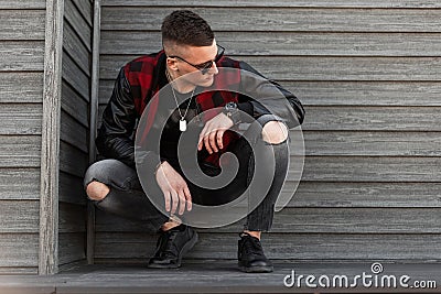 Pretty handsome young hipster man in black sunglasses in trendy red checkered jacket in sneakers in stylish ripped jeans Stock Photo