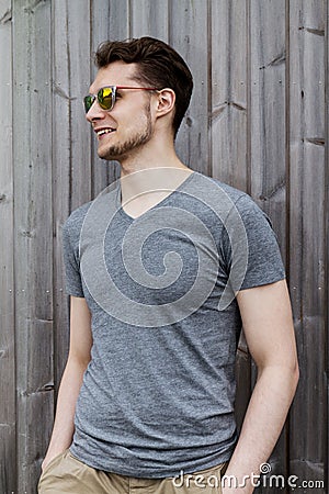Pretty handsome young man hipster with sunglasses smiling laughing behind wooden wall. Looking aside. Stock Photo