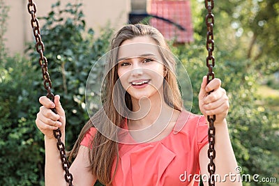 Pretty happy brunette swinging smiling near house in park on a sunny day. Stock Photo