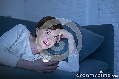 Pretty and happy red hair woman on her 20s or 30s lying on home couch or bed using mobile phone late at night smiling in internet Stock Photo