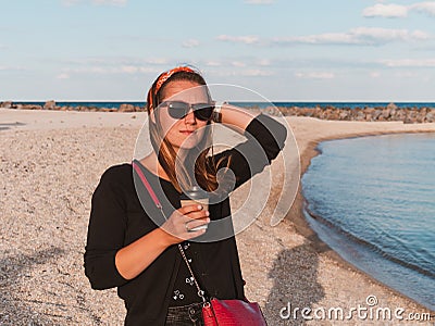 Pretty hipster woman in bandana long hair walking on sea background with coffee cup lifestyle real life travel photo Stock Photo