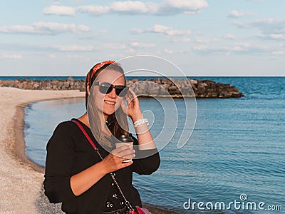 Pretty hipster woman in bandana long hair walking on sea background with coffee cup lifestyle real life travel photo Stock Photo