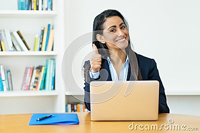 Pretty hispanic mature businesswoman at computer showing thumb up Stock Photo