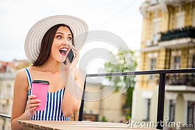 Pretty lady speaking over telephone hear great news sitting in cozy street cafe wear sun hat and striped dress Stock Photo