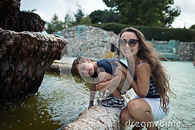 Pretty little boy with mother playing near fountain outdoor Stock Photo