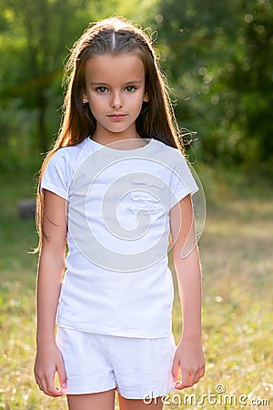 Pretty little brunette girl posing in garden, park or glade of forest. Childhood. Cute kid, outdoor portrait. Stock Photo