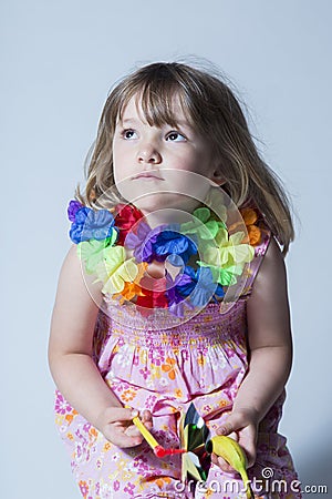 Pretty little girl dressed in pink floral dress and silk flower garland sitting on stool Stock Photo