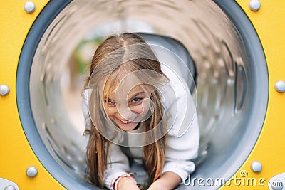Pretty, little girl, having fun, crawling on pipe on children playground. Stock Photo