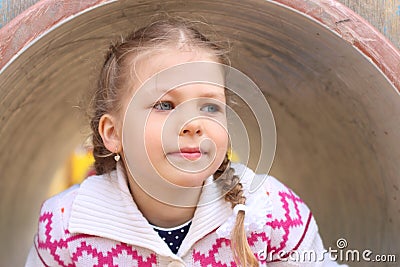Pretty little girl peeks up of pipe on playground Stock Photo