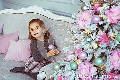 Pretty little girl sits on a sofa near Christmas tree and looks up Stock Photo