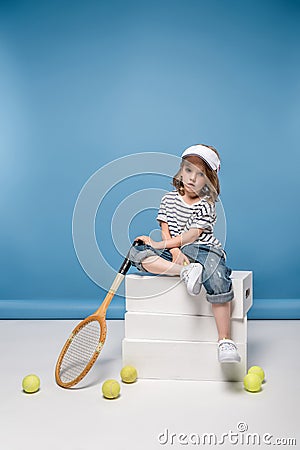 pretty little girl sitting on white boxes and holding tennis raquet Stock Photo
