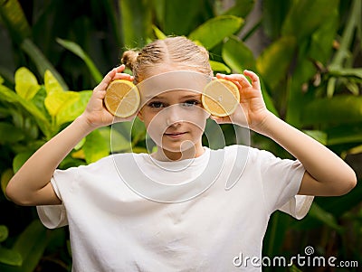 Pretty little girl with two halves of fresh lemon. Caucasian girl holding lemon near her face. Selected focus. Green tropical Stock Photo