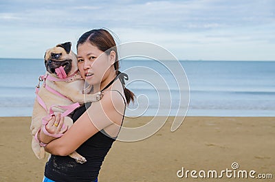 Pretty lonely asia girl hold cute dog puppy pug against beach , sea and blue sky background and smile to camera. Stock Photo