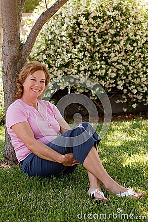 Pretty, middle-aged woman sits under tree Stock Photo