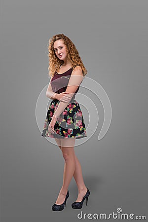 Pretty plus size young redhead and curly-haired girl wearing short skirt with floral print over gray background. Plus size Stock Photo