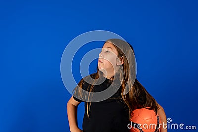 Pretty preteen girl posing funny with a soccer ball isolated on blue studio background Stock Photo