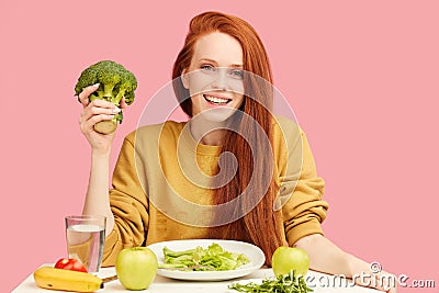 Pretty redhead caucasian woman sitting at table with healthy food and broccoli Stock Photo