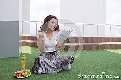 Pretty relaxed young woman reading a book at the lawn with fruit and juice Stock Photo