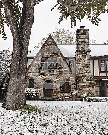 Pretty rock house with arched door and Tudor style leaded glass diamond panel windows during snowfall Stock Photo