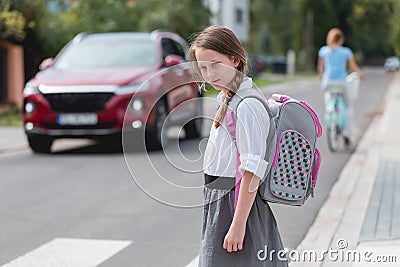 Schoolgirl with pigtails and a pink - gray backpack is standing on one-way street Stock Photo