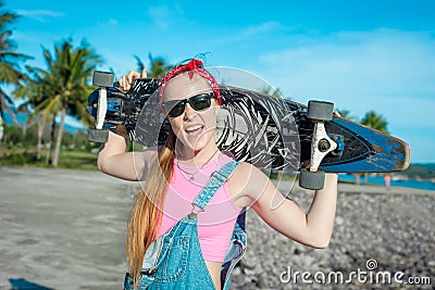 Pretty young woman stand with longboard in front of sea and palms in sunny weather. Funny smiling female. Leisure. Stock Photo