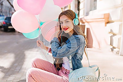 Pretty slim girl in retro outfit listening favourite song in headphones waiting for party start. Charming young woman in Stock Photo