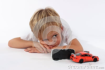 Pretty small boy lying behind crashed car toys and seeming bored or tired Stock Photo