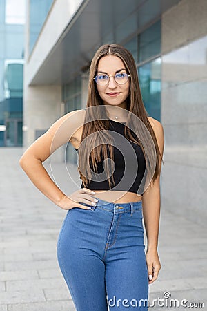 A pretty, smiling, curvy girl in glasses, black tank top, and blue jeans standing on the street Stock Photo