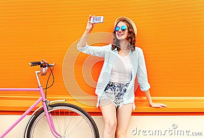 Pretty smiling young woman using taking self portrait on smartphone with retro bicycle over colorful orange Stock Photo