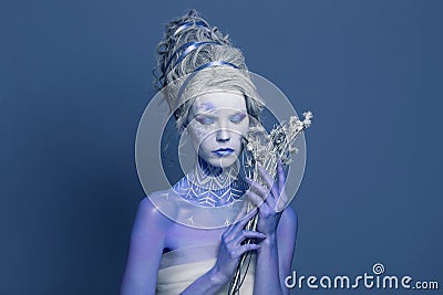 Pretty Snow Queen or Winter Witch woman with perfect fantasy makeup and painted body on blue background. Carnival and Halloween Stock Photo
