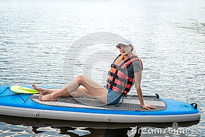 pretty sporty girl learn swim in life vest sitting with paddle on a board in city lake Stock Photo