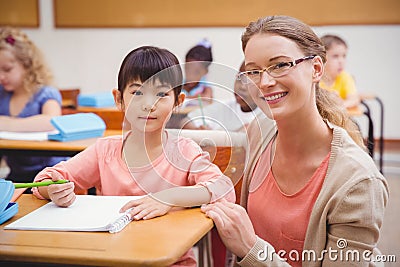 Pretty teacher helping pupil in classroom smiling at camera Stock Photo