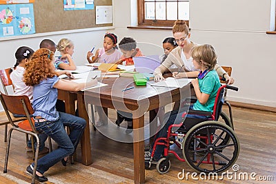 Pretty teacher helping pupils in classroom Stock Photo