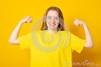 Pretty teen girl keeps fit and healthy, raises hands and shows muscles, feels proud about her achievements in gym, smiles broadly Stock Photo