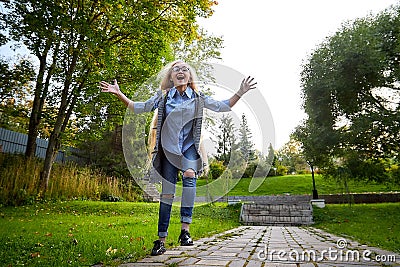 Pretty teenage girl 14-16 year old with curly long blonde hair jumping and having fun in the green park in a summer day outdoors. Stock Photo