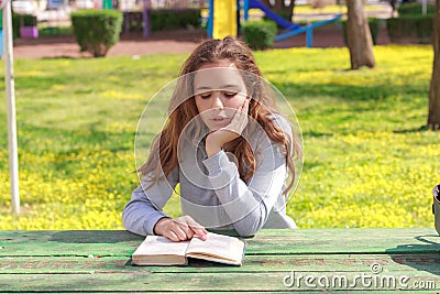 Pretty teenager girl reading a book and studying homework at the summer park Stock Photo