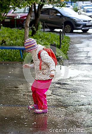 Pretty toddler girl wearing colorful raincoats and rain boots jumping in muddy puddles. Stock Photo