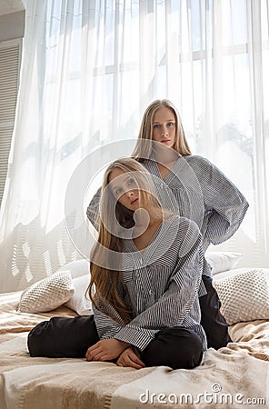 Pretty twin sisters in jeans and striped shirts with long hair sitting on bed Stock Photo