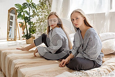 Pretty twin sisters in jeans and striped shirts with long hair sitting on sofa Stock Photo