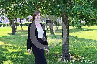 Pretty woman in black suit poses in sunny green park at su Stock Photo