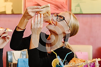 Pretty woman eating pizza. Girl wearing glasses, golden ring and bracelet on her hand. She has ponytail. Enjoying the Stock Photo