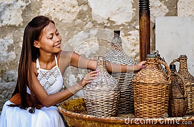 Pretty woman in ethnic Mediterranean folk traditional costume holding a rattan olive oil jug. Hospitality and ethnic tourism conce Stock Photo