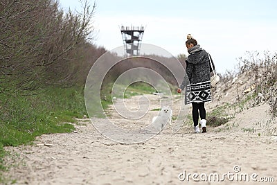 Pretty woman with her dog out in the park. Puppy white dog is running with it`s owner. Stock Photo