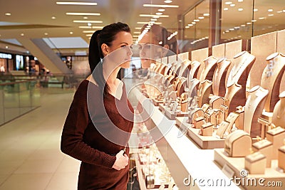 Pretty woman looking at jewelry in store window. Customer near jewellery. Dreamy long haired girl chooses silver, gold, diamonds, Stock Photo