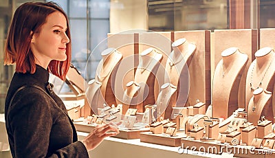 Pretty woman looking at jewelry in store window. Customer near jewellery. Dreamy red hair girl chooses silver, gold, diamonds, Stock Photo