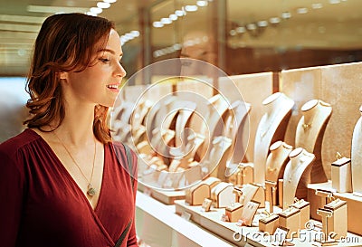 Pretty woman looking at jewelry in store window. Smiling interested customer near jewellery. Girl chooses gold, diamonds or Stock Photo