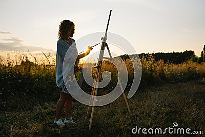 Pretty woman is painting. Open air session. Cute woman draws a picture at sunset. girl artist Stock Photo