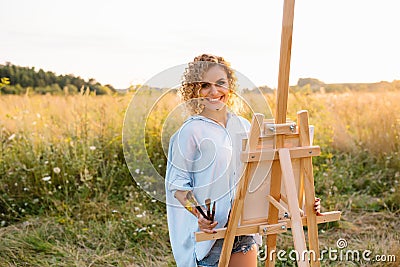 Pretty woman is painting. Open air session. Cute woman draws a picture at sunset. girl artist. Stock Photo