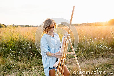 Pretty woman is painting. Open air session. Cute woman draws a picture at sunset. girl artist Stock Photo