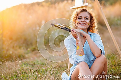 Pretty woman is painting. Open air session. Cute woman draws a picture at sunset. girl artist. Stock Photo